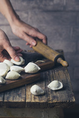 The process of making homemade dumplings. Raw homemade dumplings with meat on a wooden board with women hands