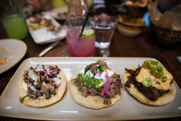 Three modern tex mex taco appetizers on a plate with a margarita in the background 