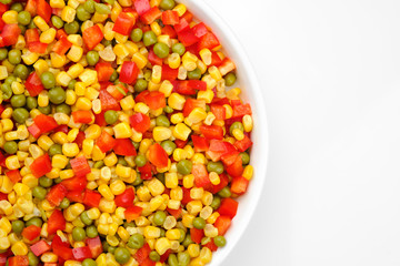 a mix of chopped vegetables paprika, corn, peas in white plate top view