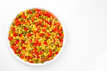 a mix of chopped vegetables paprika, corn, peas in white plate top view