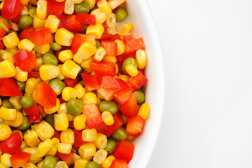 a mix of chopped vegetables paprika, corn, peas in white plate top view