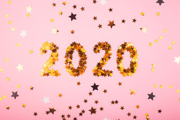 The numbers 2020 are laid out from golden glowing stars on a bright pink background among different stars. Winter holidays and christmas overlay. Top view, flat lay.