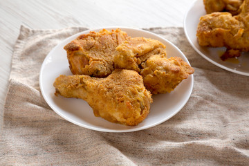 Tasty homemade oven baked fried chicken on a white plate over white wooden surface, low angle view. Close-up.