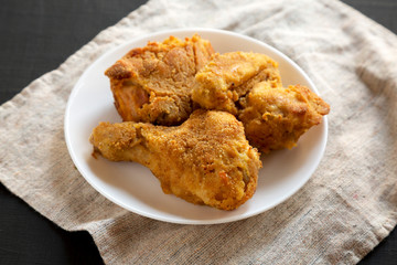 Delicious homemade oven baked fried chicken on a white plate over black background, low angle view. Close-up.