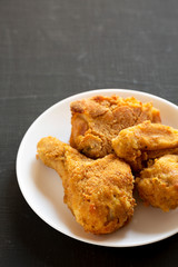 Delicious homemade oven baked fried chicken on a white plate over black background, low angle view. Copy space.