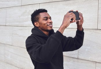 Young smiling african man taking selfie picture by phone on city street over gray wall background - Powered by Adobe