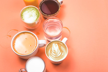 Different drinks cappuccino, tea, sea buckthorn juice, milk, water, orange juice and matcha on a bright coral pink background. Top view, flat lay, copy space.