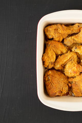 Delicious homemade oven baked fried chicken in a dish over black background, top view. Flat lay, overhead, from above. Copy space.