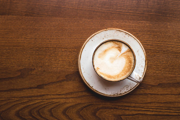 Cappuccino in rustic cup and dish on a brown coffee shop table. Top view, flat lay.