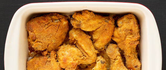 Delicious homemade oven baked fried chicken in a dish over black surface, top view. Flat lay, overhead, from above.