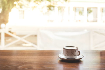 Rustic cup of cappuccino with saucer on a wooden table of a coffee shop by the window with bright sunlight. Copy space.