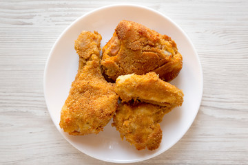 Delicious homemade oven baked fried chicken on a white plate on a white wooden surface, top view. Overhead, from above, flat lay. Close-up.