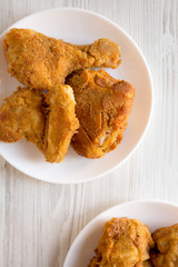 Delicious homemade oven baked fried chicken on a white plate on a white wooden table, top view. Overhead, from above, flat lay. Close-up.