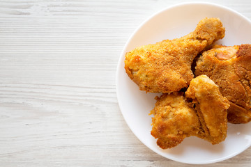 Delicious homemade oven baked fried chicken on a white plate on a white wooden background, top view. Overhead, from above, flat lay. Copy space.