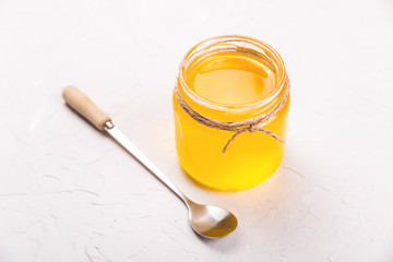Ghee or clarified butter in a glass jar on a neutral textured background next to a spoon.