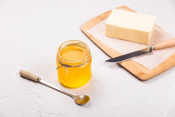 Ghee or clarified butter in a glass jar on a neutral textured background next to a spoon.