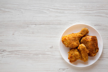 Tasty homemade oven baked fried chicken on a white plate on a white wooden background, top view. Overhead, from above, flat lay. Copy space.