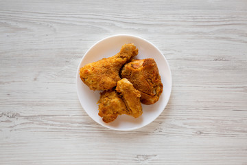 Delicious homemade oven baked fried chicken on a white plate on a white wooden table, top view. Overhead, from above, flat lay.