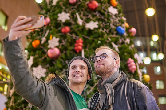 homosexual couple of boys, taking a selfie, in front of a Christmas tree, inside a mall