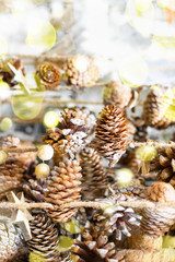 Christmas eco garland of pine cones and wooden stars hanging on a jute rope with bokeh lights, holiday decoration background made of natural materials, copy space.