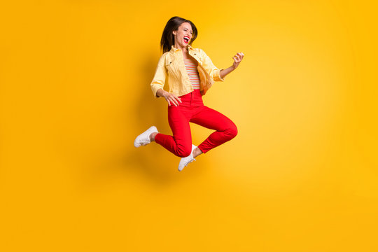 Full length body suze turned photo of cheerful rude excited crazy overjoyed woman rejoicing in jumping playing imagine guitar in red pants isolated vivid color background