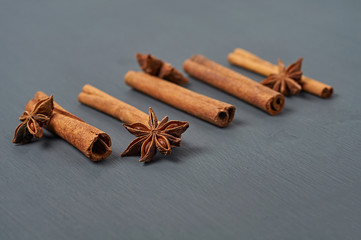 Row of five flavour cinnamon sticks near stars of anise lies on dark scratched desk on kitchen. Close-up