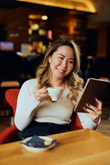 Beautiful Asian woman drinking coffee and looking at her tablet