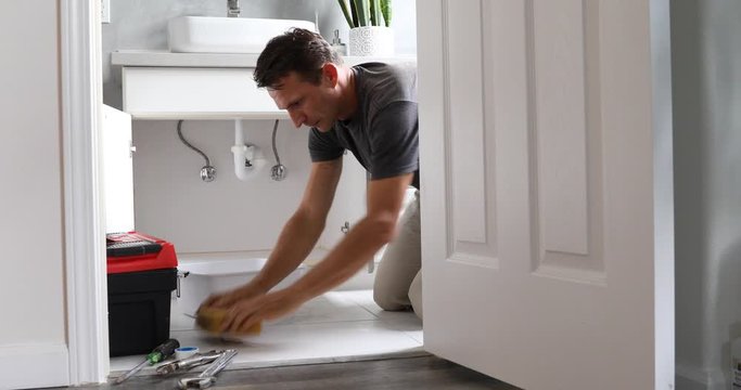 Man At Home Mopping Up Water From Leaking Pipe in Bathroom