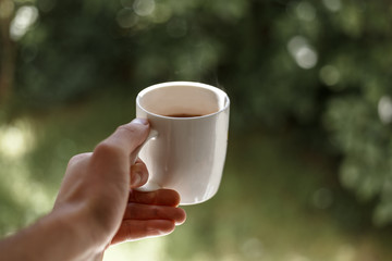 Close up of a man holding cup of coffee in the morning. Natural green background. Morning ritual 
