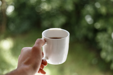 Close up of a man holding cup of coffee in the morning. Natural green background. Morning ritual 