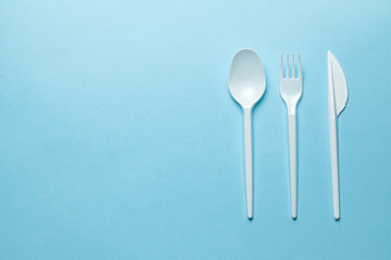 Plastic cutlery, forks, spoons and knives. Pollution of the environment with plastic and microplastics. Blue background. Copy space for text.