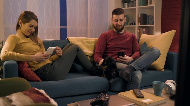 Young couple chatting with their mobile devices and ignoring each other