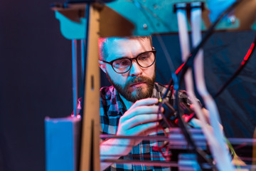 Young male designer engineer using a 3D printer in the laboratory and studying a product prototype,...