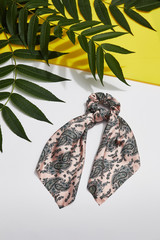 Subject shot of a pink satin hair scarf fixed on the scrunchie with black Paisley print. The...