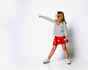 casual little girl in a red skirt pointing and looking to her side with a smile.