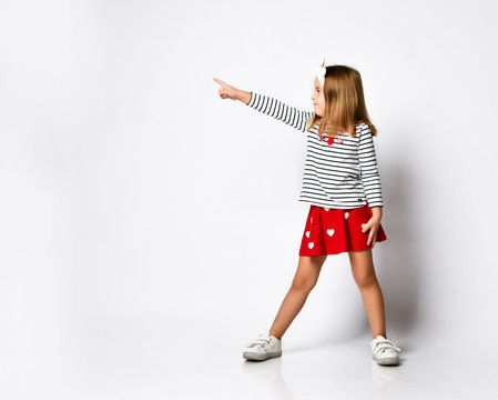 casual little girl in a red skirt pointing and looking to her side with a smile.