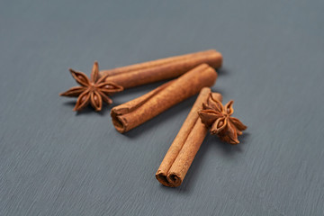 Three flavour cinnamon sticks near stars of anise lies on dark scratched desk on kitchen. Close-up