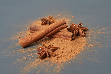 Two flavour cinnamon sticks beside brown powder and stars of anise lies on dark scratched desk on kitchen. Close-up
