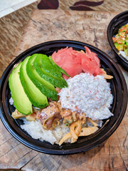 Spicy tuna and salmon poke bowl with avocado, ginger, onions, and white rice, sitting on a wooden table