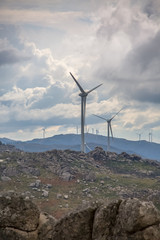 View of a wind turbines on top of mountains, cloudy sky as background