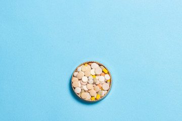 Bowl with pills of different types on a blue background. The concept of insomnia, vitamins. Flat lay, top view