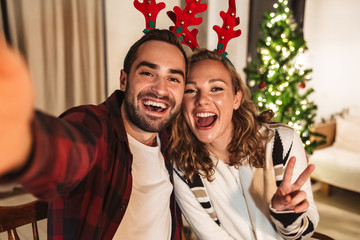 Photo of young pleased couple taking selfie and gesturing peace sign