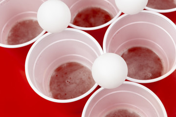 Cups and plastic ball on red background. Beer pong game