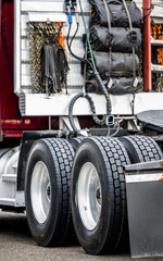 Fototapeta na wymiar Back of the big rig semi truck with wheel axels and accessories with cargo cover and rubber fasteners and safety chains