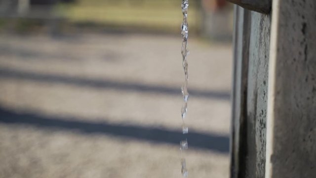 Jib down of stream of water falling from wolfshead shaped faucet into small stone reservoir