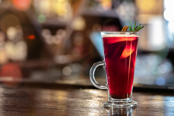 Mulled wine with spices, cinnamon and dried flowers of star anise on wooden bar counter in restaurant, blurred background with bokeh lights, copy space, Christmas cocktail for New Year