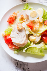 Grilled chicken vegetables and egg salad in a white plate on a concrete background .