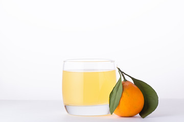 Refreshing mandarin soda drink or juice in a glass with citrus fruits on white background close up. Mandarins with green leaves and yellow, orange drink on white table, copy space