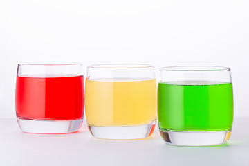 Glasses of various colors and tastes soda drink on white background. Red, yellow, green soda or sparkling water close up on white table, copy space