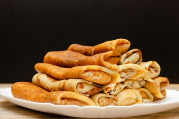 Many homemade thin pancakes with filling stacked pyramid on a white plate against a black wall, copy space